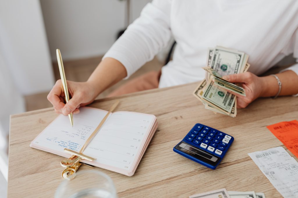 Utang Tanpa Perjanjian Tertulis: Bagaimana Pembuktiannya Menurut Hukum Indonesia? Adult holding cash and writing in planner while using a calculator at home.